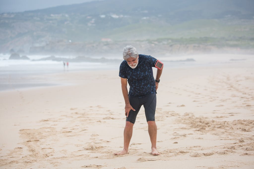 Elderly man stretching on a sandy beach in Portugal, promoting healthy lifestyle.