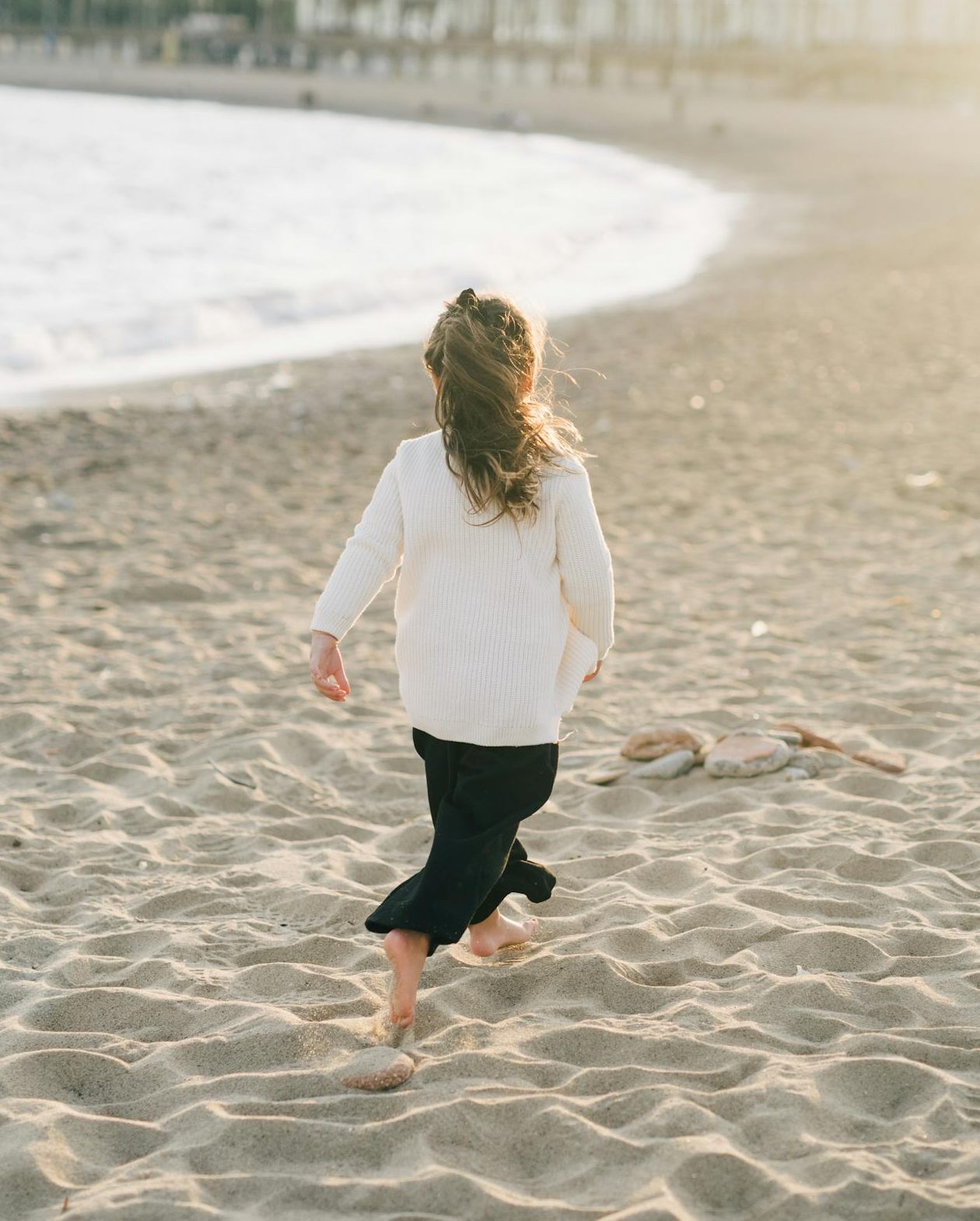 Young girl enjoying a serene sunset walk on the sandy oceanside beach, capturing the essence of seaside leisure.